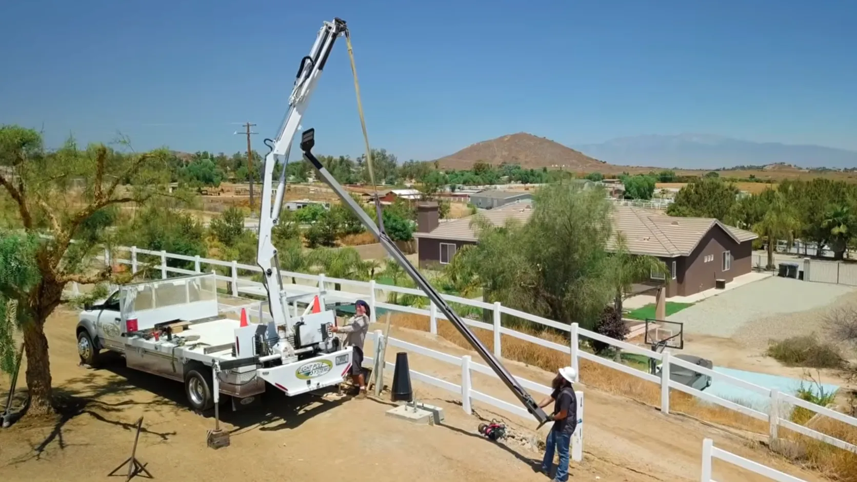 Utility crew safely lifting a steel light pole with a crane in a controlled work area